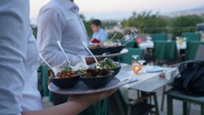A person holding a tray with bowls of food, a table with chairs, and a view of the outdoors. - Belizi Hotel (Urla)