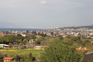 A coastal town with a mix of residential buildings and greenery, a clear view of the sea, and a distant mountain range. - Belizi Hotel (Urla)