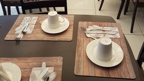 A dining area with tables set for two, each with white cups, plates, and cutlery. - Channel View Lodge (Kempton Park)