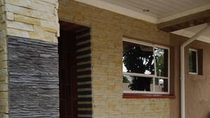 A modern building entrance with a stone facade, a wooden door, and a window with a view of trees. - Channel View Lodge (Kempton Park)