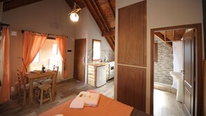 A cozy room with a wooden dining table, a small kitchen area, and a bathroom with a sink and toilet.