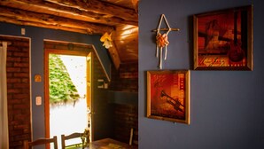 A rustic interior with a wooden ceiling, a brick wall, and a dining area with a table and chairs. There are framed pictures on the wall, including one of a guitar and another with a trumpet.