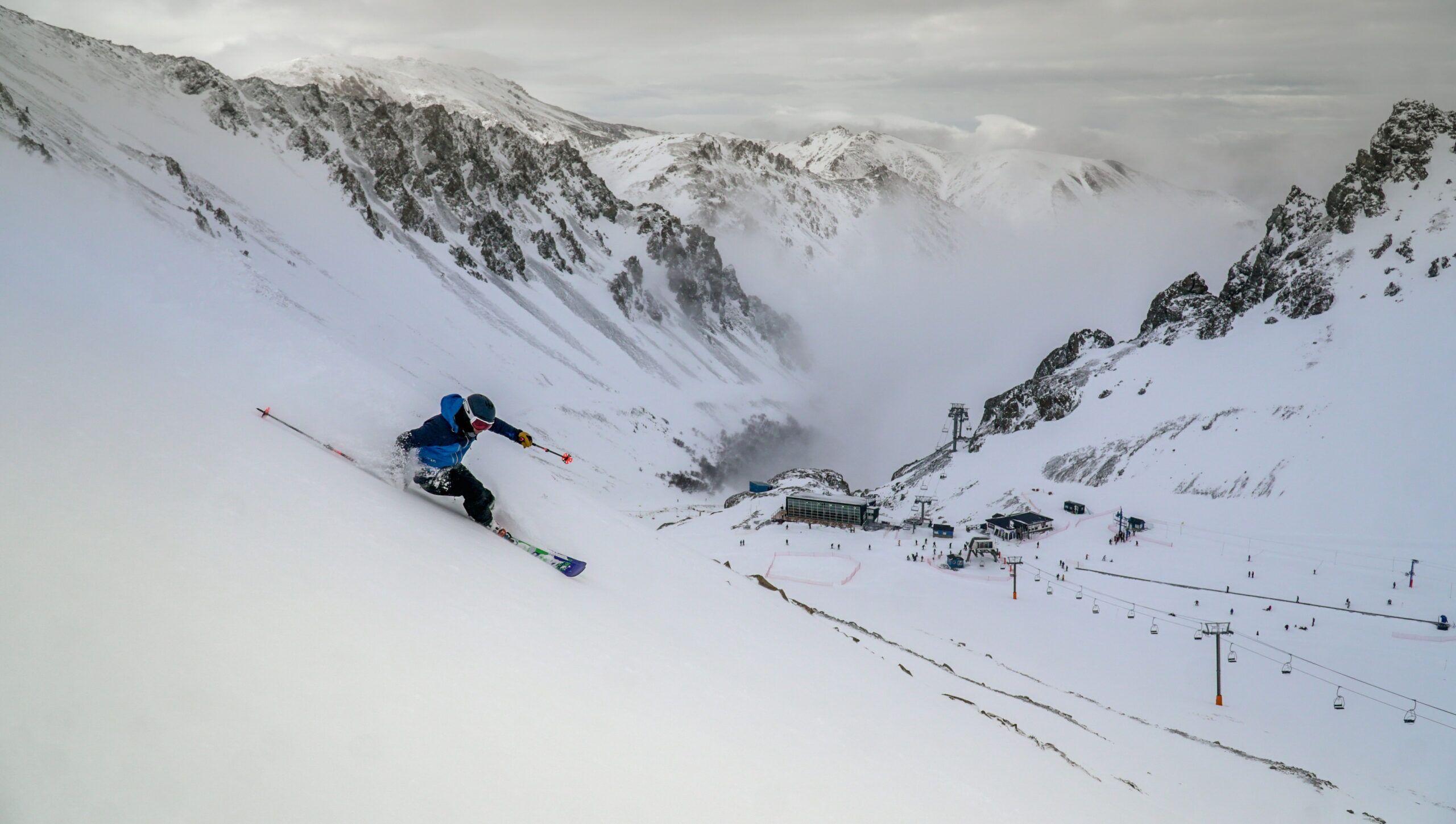 A ski slope with a skier in motion, a ski lift, and a building in the background.