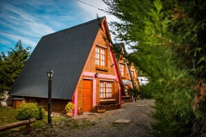 A two-story house with a steeply pitched roof, a wooden door, and a window with a wooden frame. - Cabañas Patagonia Encantada by DECK (Esquel)