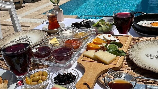 A poolside dining setup with a table set for a meal, including watermelon, cheese, and various condiments. - Cunda Paradise Otel (Ayvalik)