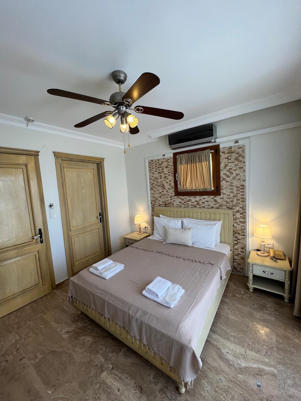 A hotel room with a bed, two nightstands, a ceiling fan, and a wall-mounted air conditioner.
