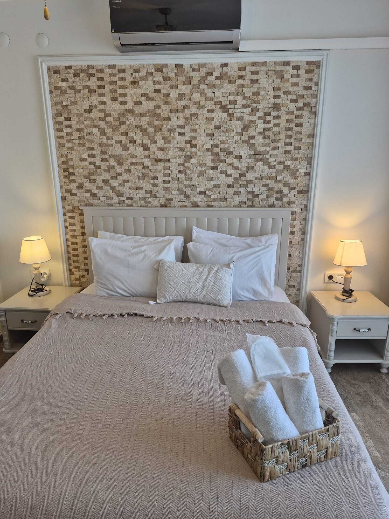 A neatly made bed with a textured blanket, a headboard with a mosaic pattern, and a basket of towels on the floor.