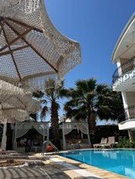 Área de piscina com céu azul límpido, palmeiras e um edifício com varanda.
