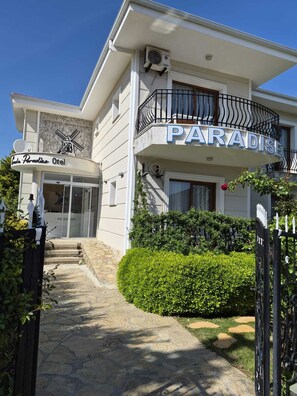 Un hotel llamado 'Paradise' con una recepción, un letrero con forma de molino y un jardín bien cuidado.