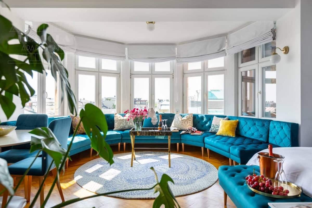 Ein modernes Wohnzimmer mit einem blauen Ecksofa, einem runden Couchtisch und großen Fenstern mit Blick auf die Stadt.