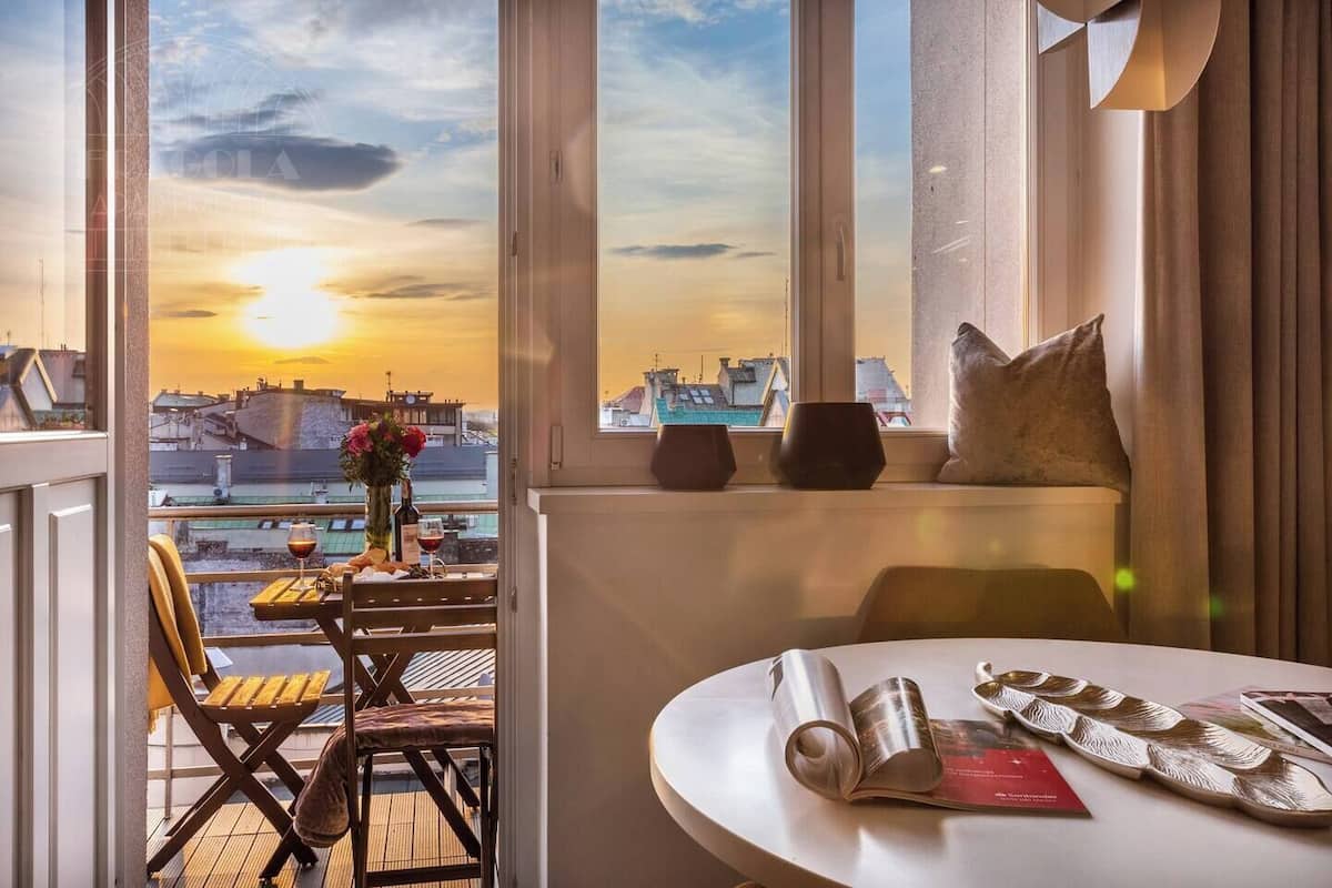 Ein Zimmer mit Blick auf einen Sonnenuntergang, ein Tisch mit einem Buch, ein Stuhl und ein Fenster mit einem Kissen.