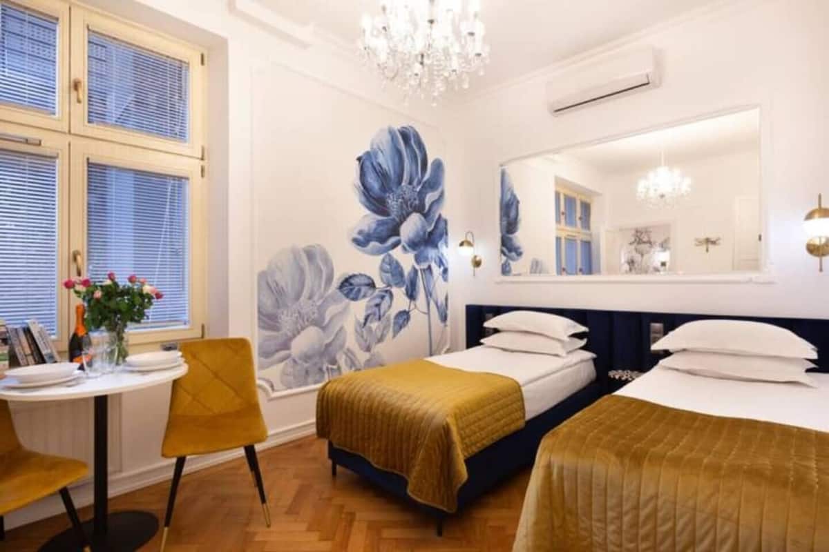 Une chambre avec deux lits, une table à manger, des chaises, une grande fresque murale à motifs floraux et un lustre.
