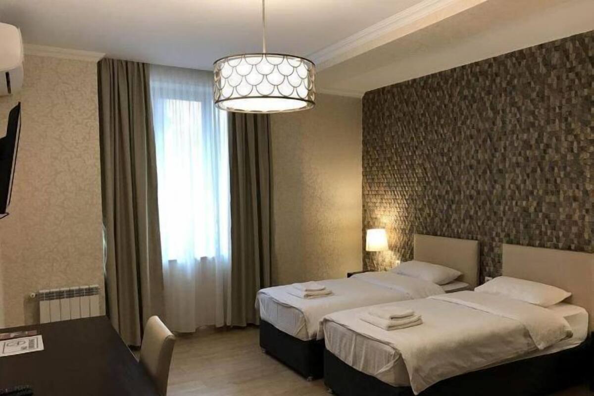 Een hotelkamer met twee bedden, een bureau, een stoel, een lamp en een kamer met een patroon op de muur.