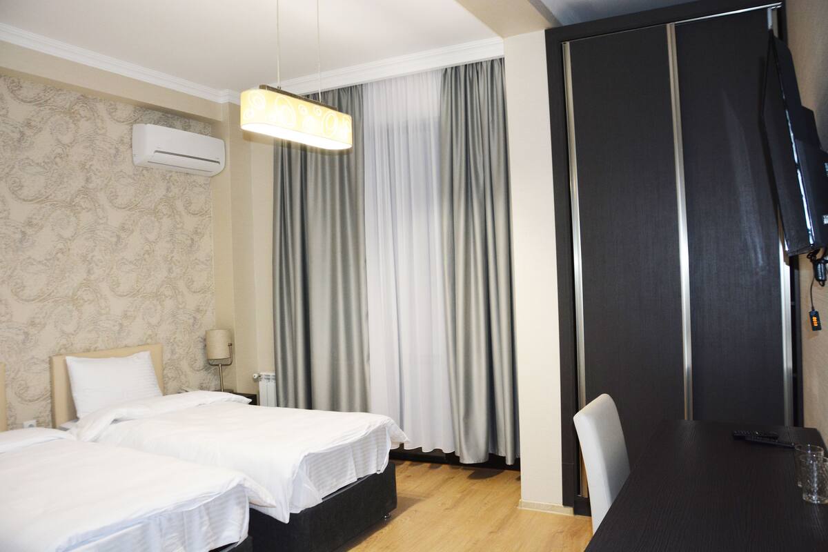 Een hotelkamer met twee bedden, een bureau, een stoel, een televisie en een raam met gordijnen.