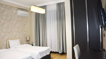 Habitación de hotel con dos camas, un escritorio, una silla, un televisor y una ventana con cortinas.