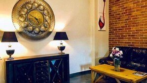 Una sala de estar con un reloj de pared redondo, dos lámparas, un sofá de cuero negro, una mesa de centro de madera y una pared de ladrillo.