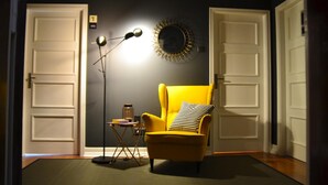 A room with a yellow armchair, a floor lamp, a small side table, and a wall-mounted mirror. - Archisuites (Coimbra)