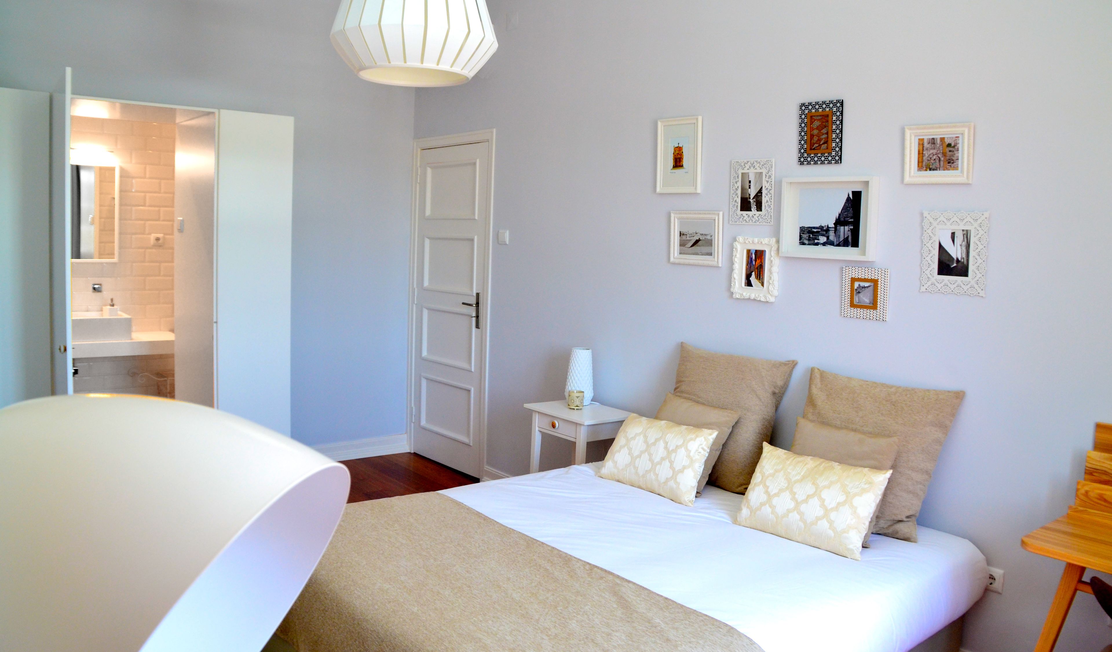 Quarto com cama, mesas de cabeceira, abajur e quadros na parede.