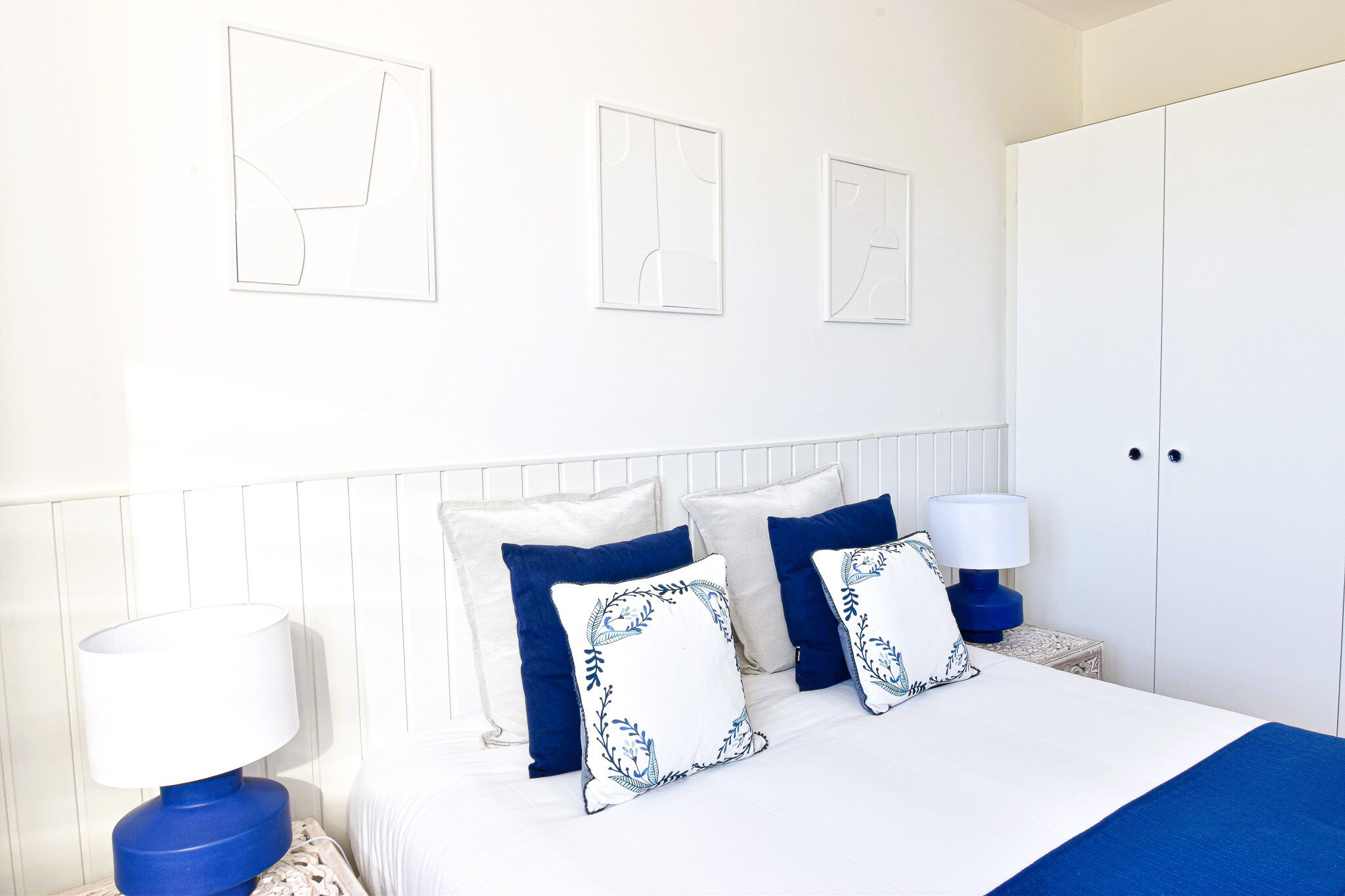 A bedroom with a bed, pillows, a nightstand, a lamp, and a wardrobe.