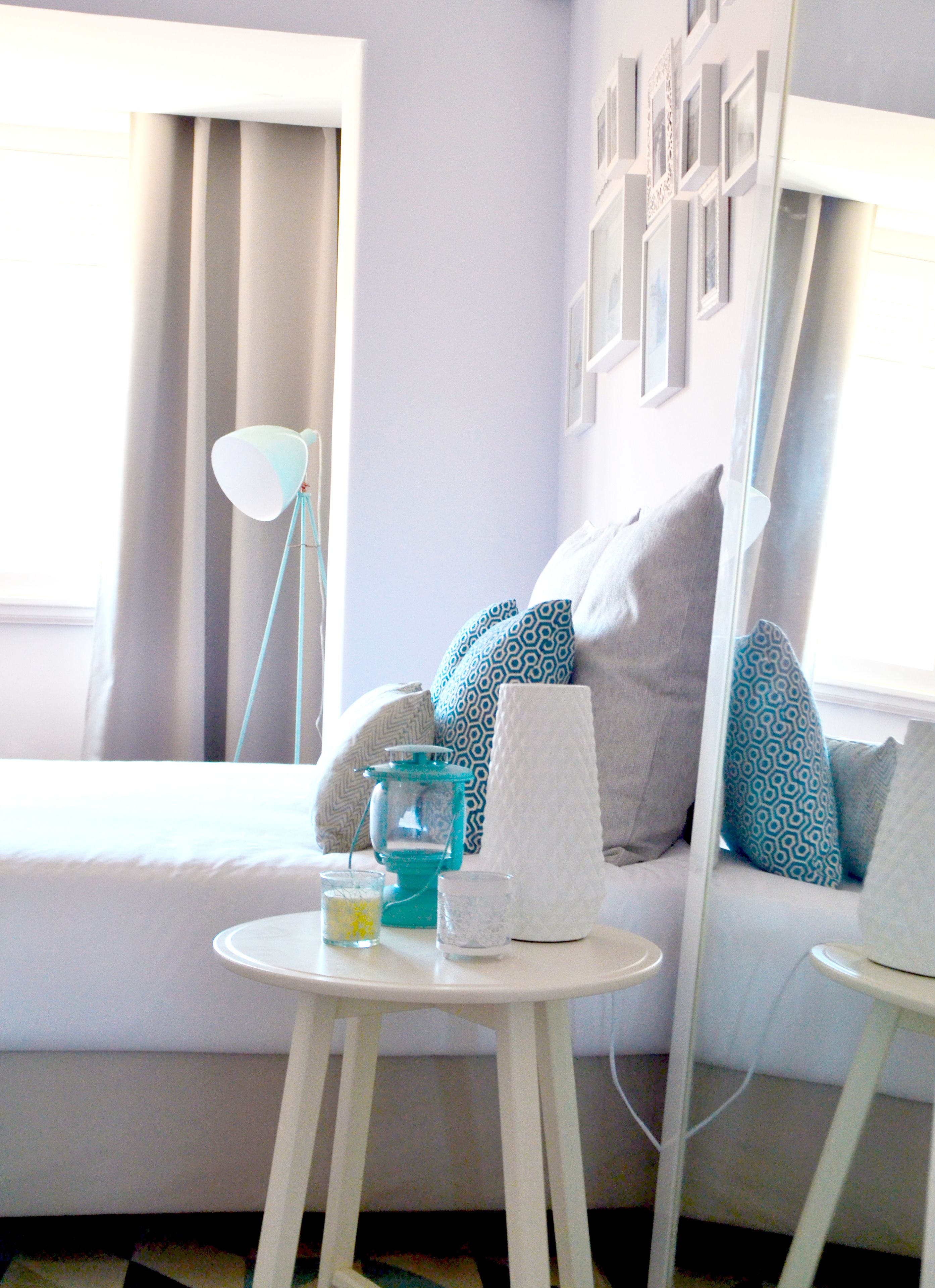 Habitación de hotel moderna con una cama, una mesa redonda blanca, una lámpara azul y un espejo que refleja la decoración de la habitación.