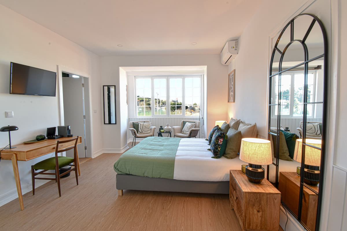 A bedroom with a bed, a desk, a chair, a lamp, and a large mirror.