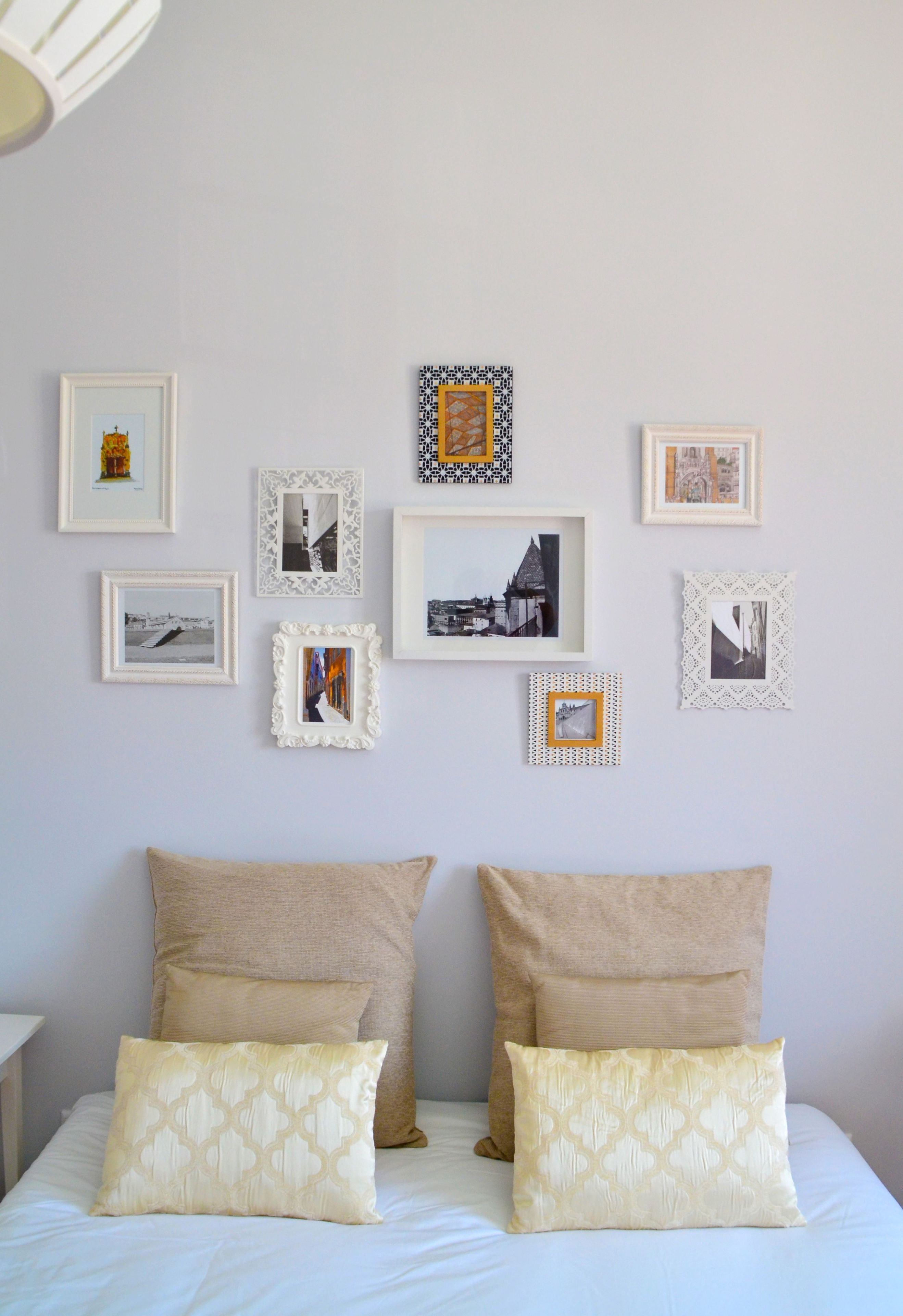 A bedroom with a bed, two pillows, and a wall decorated with framed pictures.
