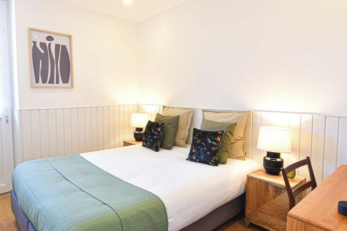 A neatly arranged bedroom with a bed, bedside tables, a chair, and a framed picture on the wall.