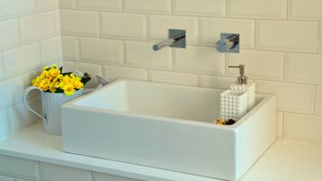 Une baignoire rectangulaire blanche, dotée d’un robinet argenté et d’un distributeur de savon, le tout posé sur un plan de travail blanc.