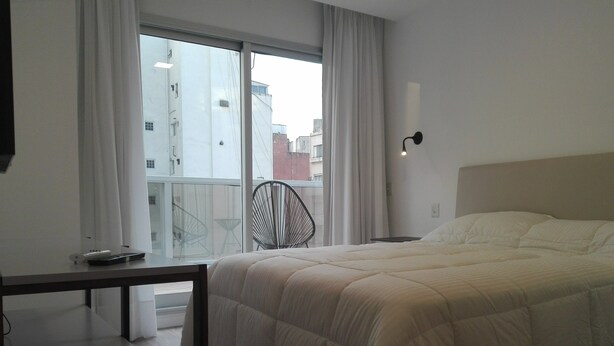 Ein Hotelzimmer mit Bett, Schreibtisch, Stuhl und einem fenster mit Vorhängen.