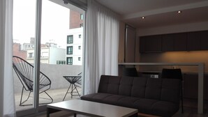 Eine moderne Wohnung mit einer Couch, einem kleinen Tisch und einem Balkon mit Stühlen.