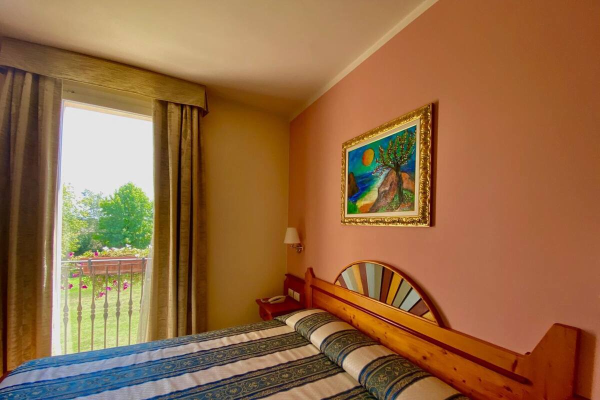 A hotel room with a bed, a painting on the wall, and a view of the outdoors.