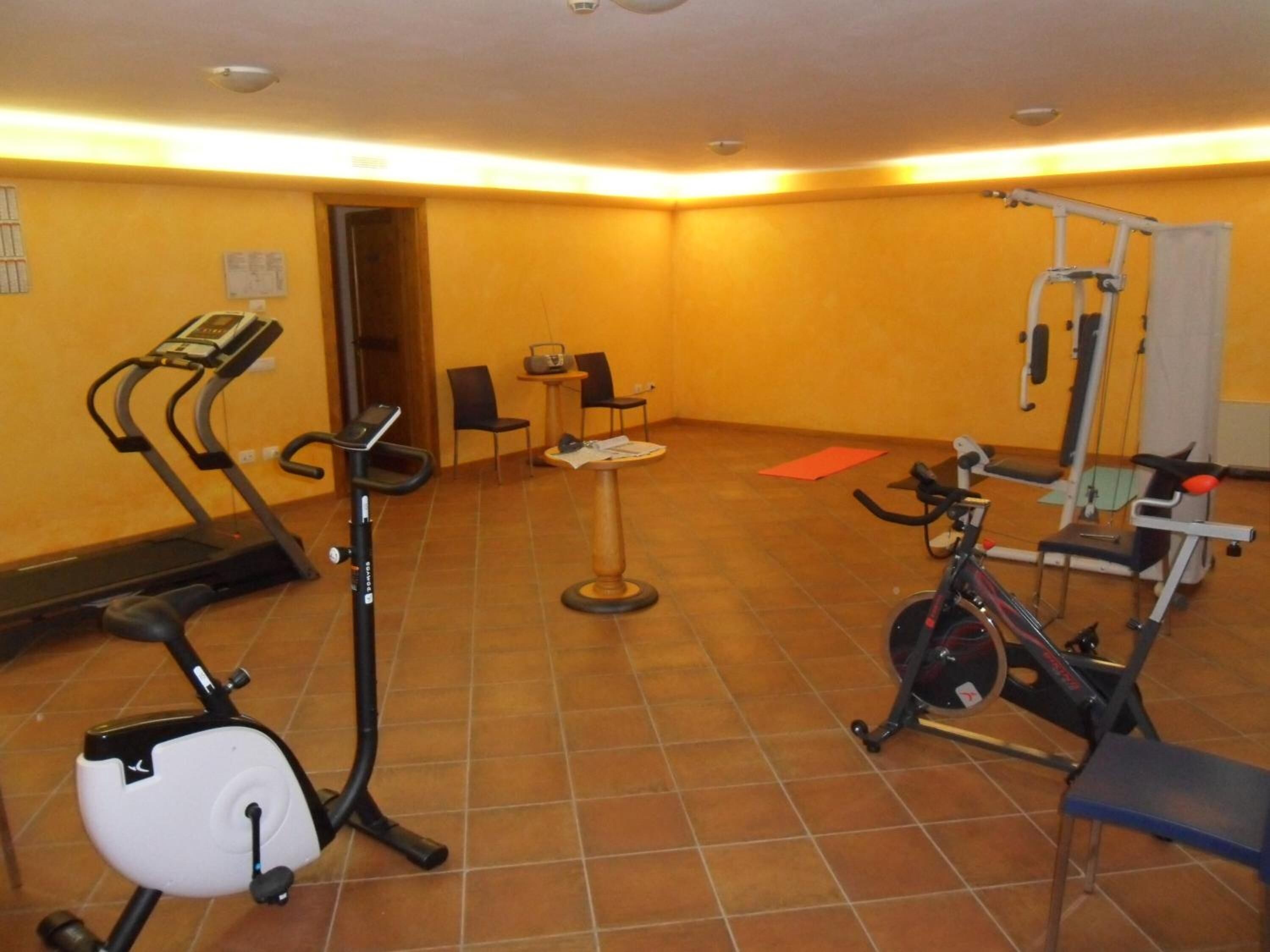 A gym with exercise equipment including treadmills, an elliptical, and a stationary bike. There are chairs and a small table in the room.