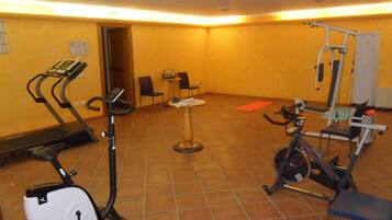 A gym with exercise equipment including treadmills, an elliptical, and a stationary bike. There are chairs and a small table in the room.