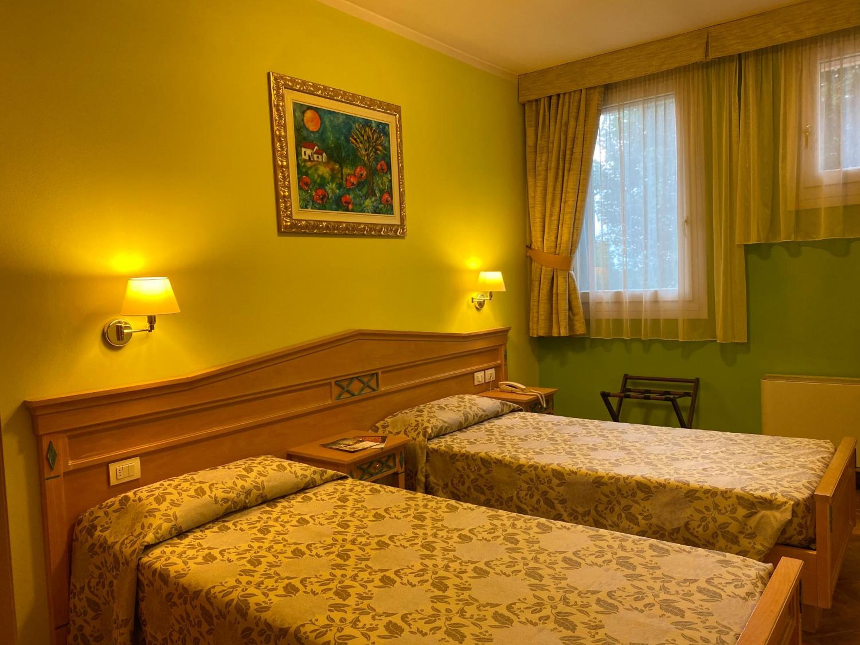 A hotel room with two beds, a painting on the wall, and a window with curtains.