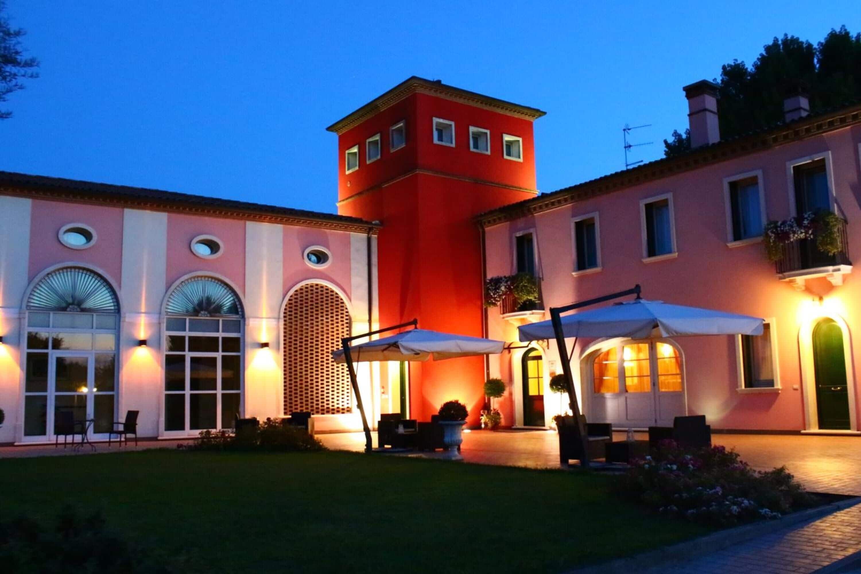 Ein Gebäude mit einem roten Turm, Bogenfenstern und einer Terrasse mit Sonnenschirmen.