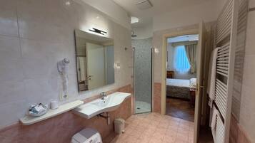 Une salle de bain moderne avec un lavabo, un miroir, une douche et une chambre à coucher visible à travers une porte ouverte.