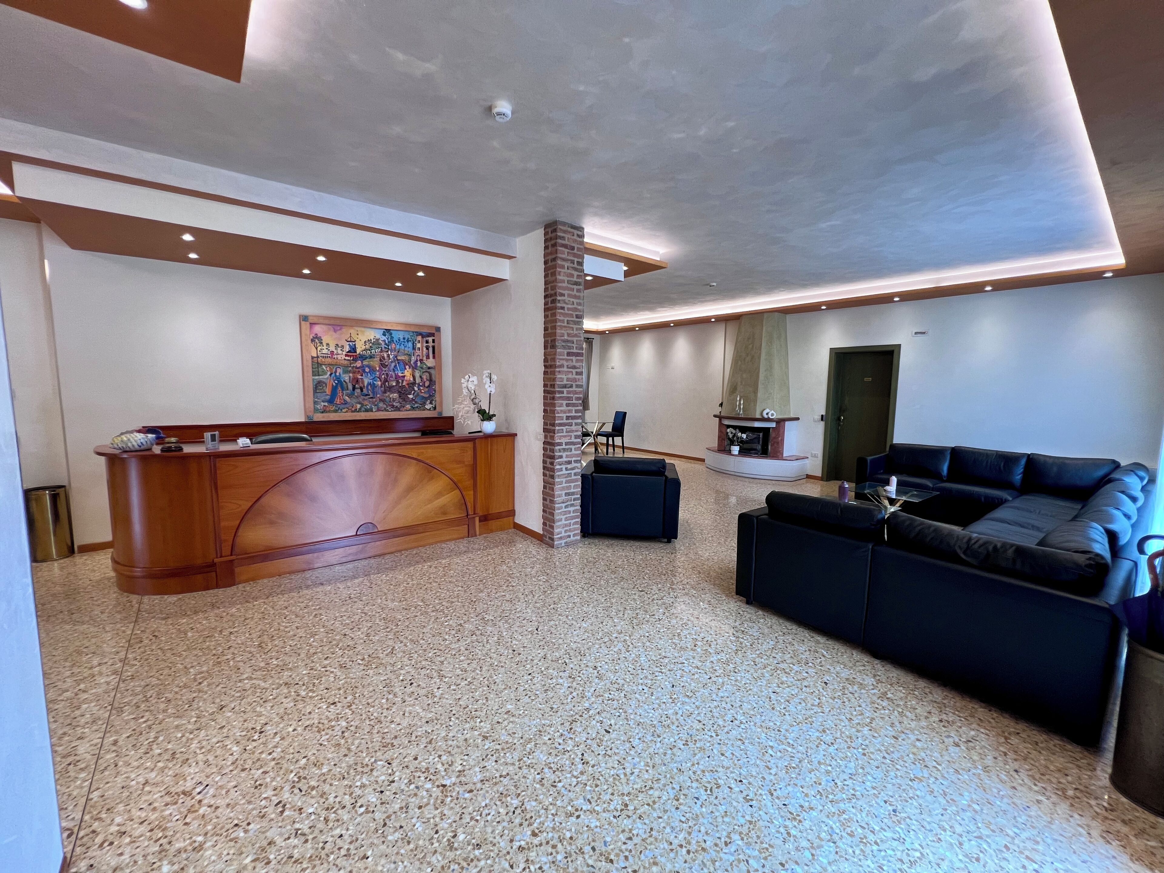 A spacious lobby with a reception desk, a fireplace, a sofa, and a large painting on the wall.
