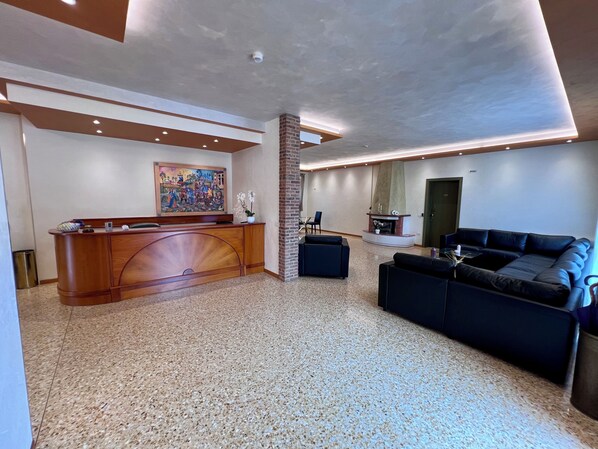 A spacious lobby with a reception desk, a fireplace, a sofa, and a large painting on the wall.