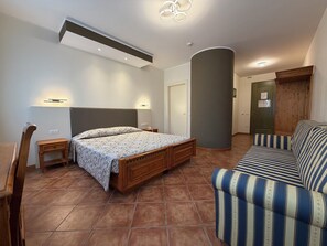 A bedroom with a bed, a nightstand, a sofa, a wooden chair, a curved wall, and a door.