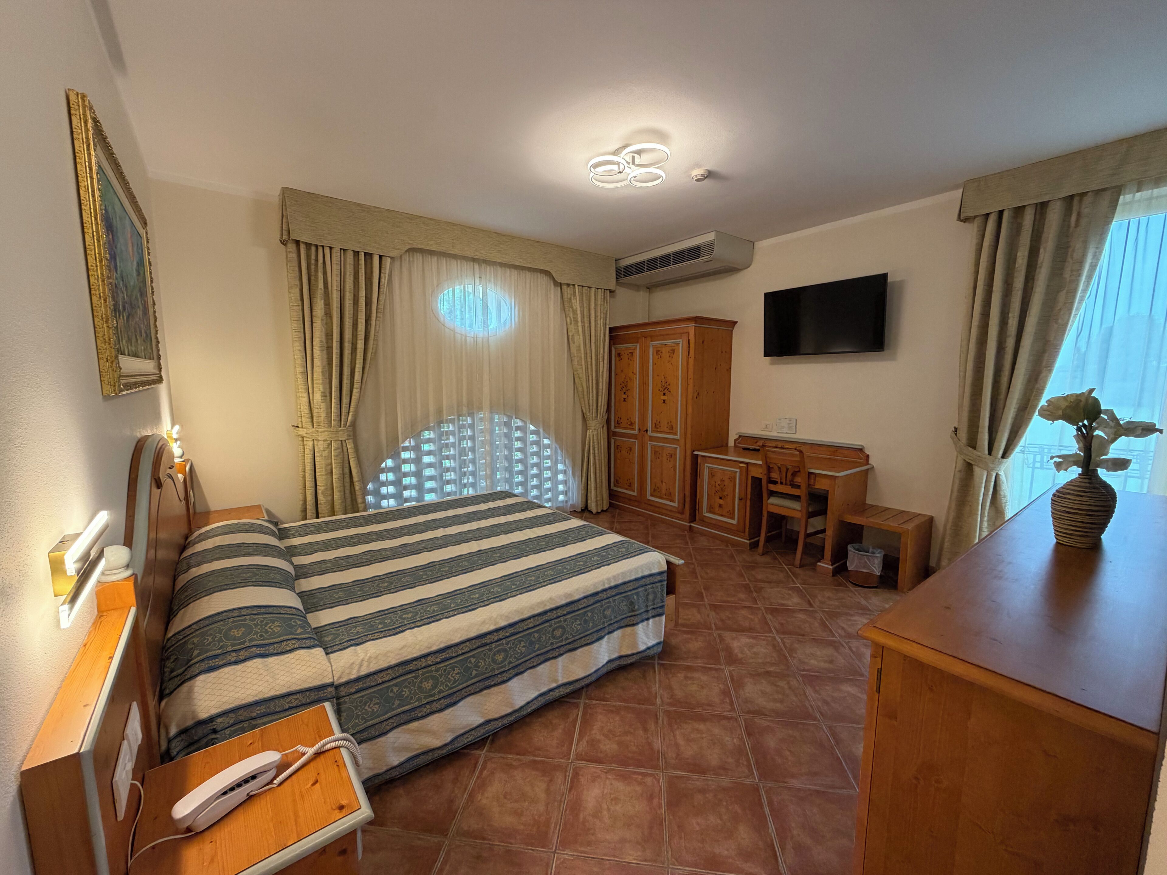 Een hotelkamer met een bed, een bureau, een televisie en een raam met gordijnen.