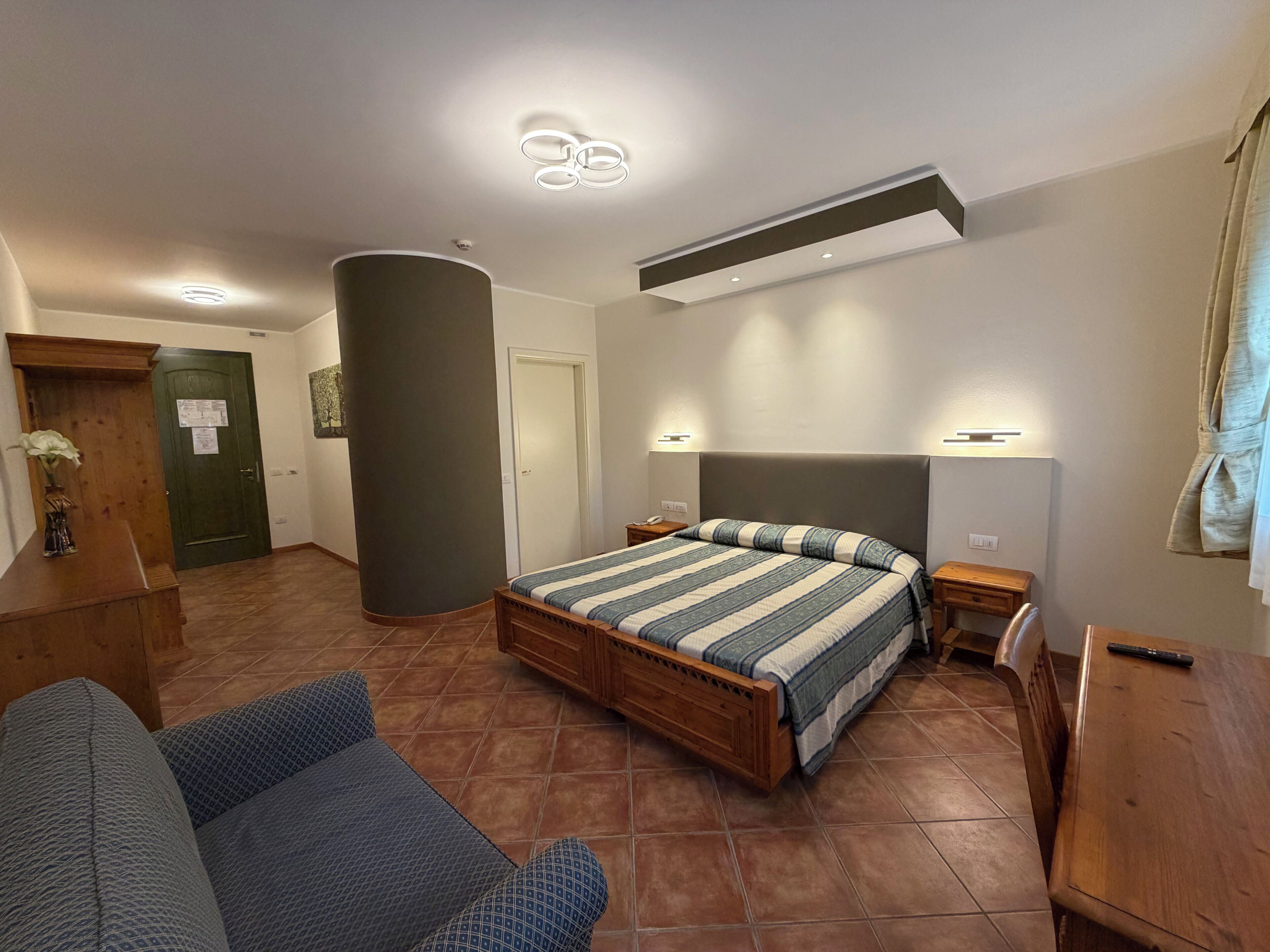 Ein Schlafzimmer mit einem Bett, einem Schreibtisch, einem Sessel, einer Couch und einer großen Säule.