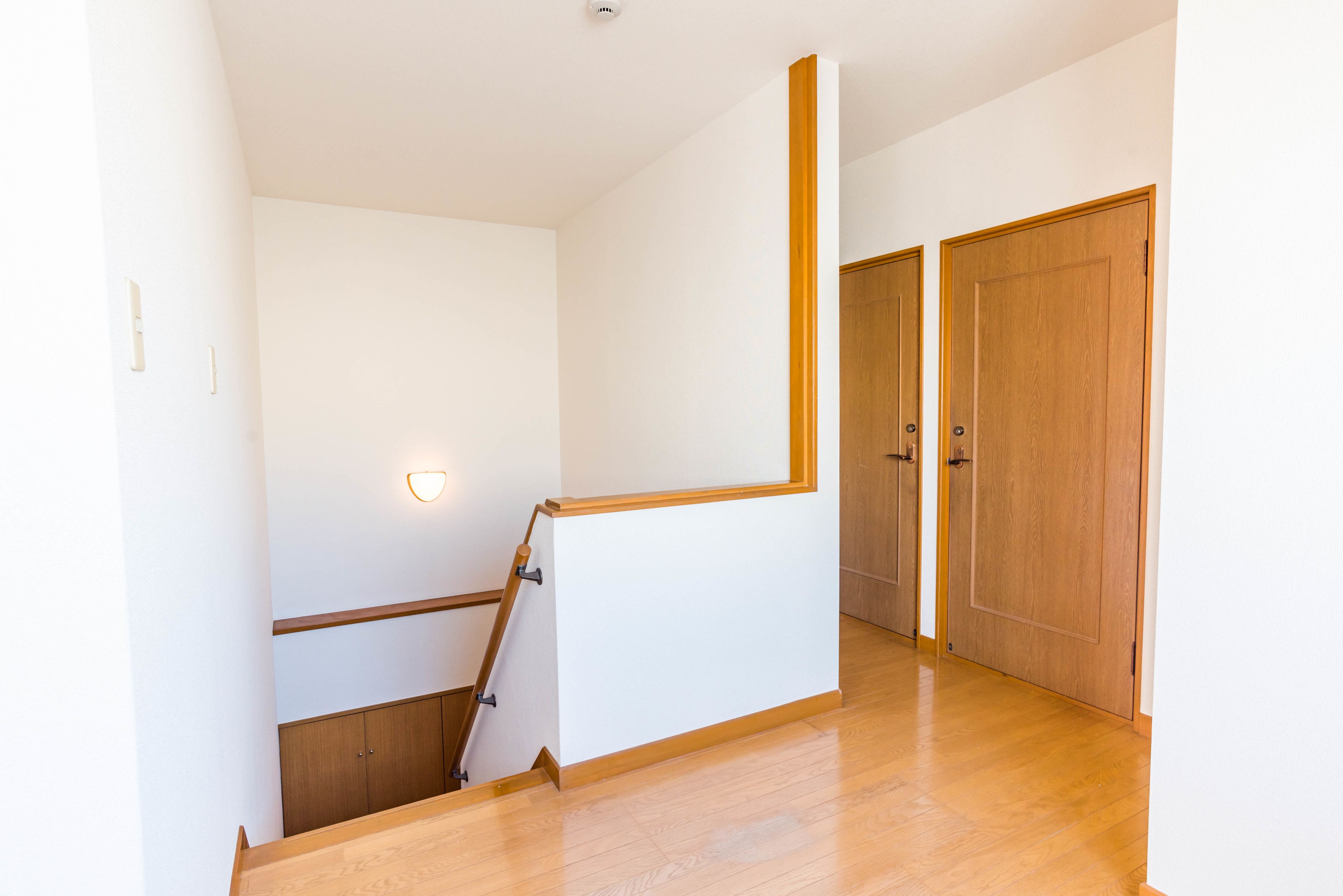 A hallway with wooden flooring, white walls, and wooden doors.