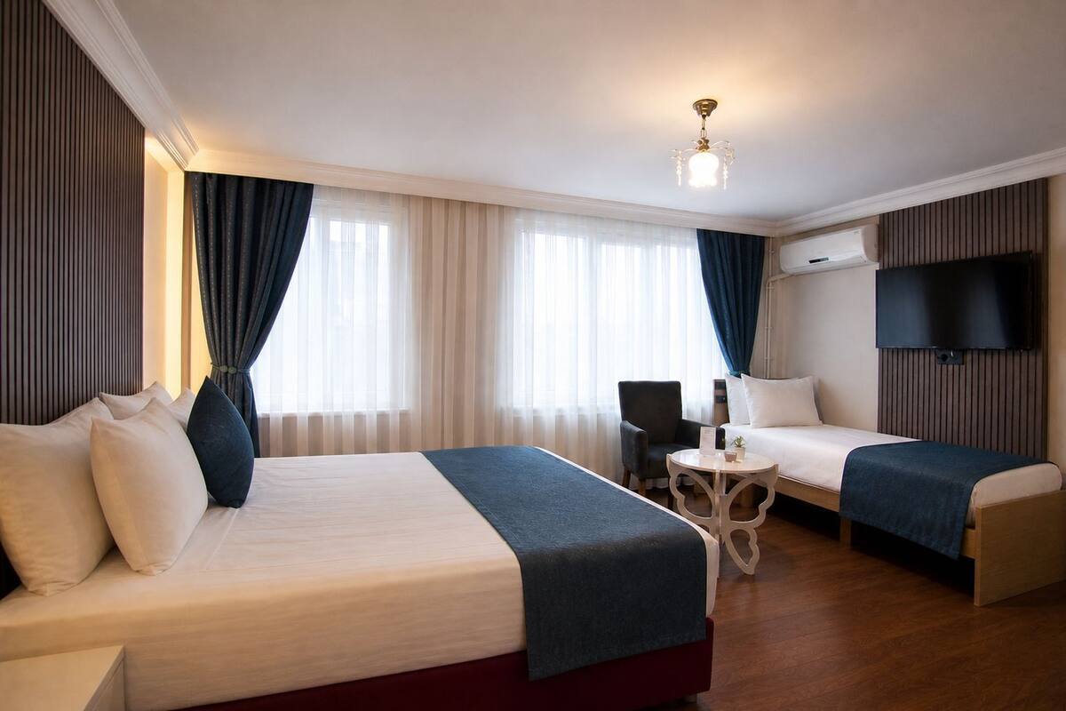 Une chambre d’hôtel avec deux lits, une petite table, une chaise, un téléviseur et un luminaire au plafond.
