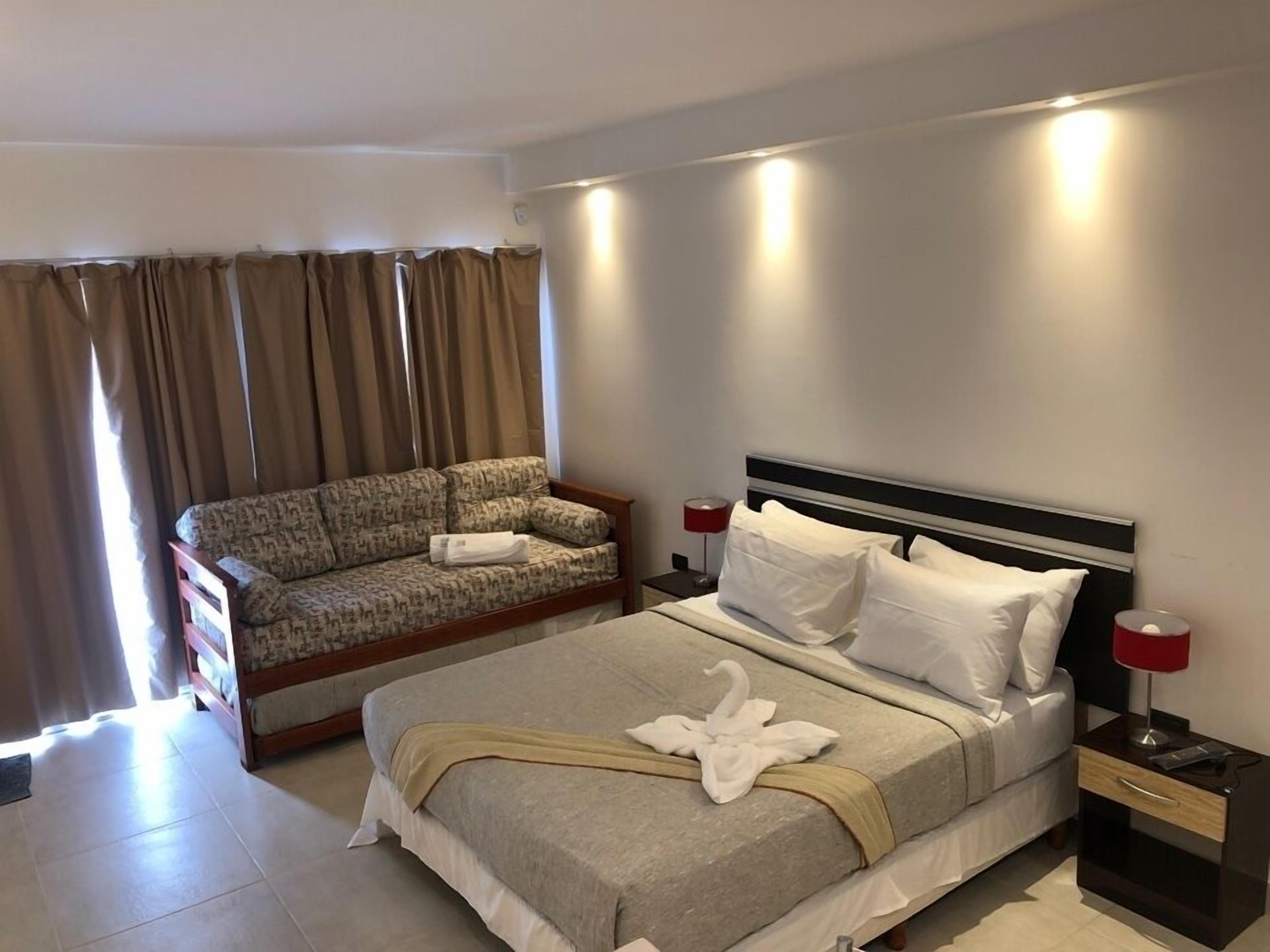 Quarto de hotel com cama, sofá, mesa de cabeceira e abajur.