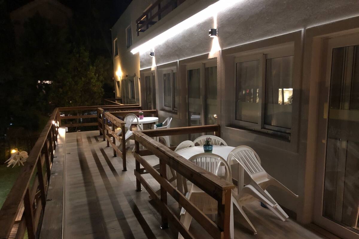 An outdoor patio with wooden railings, white plastic chairs, and tables.