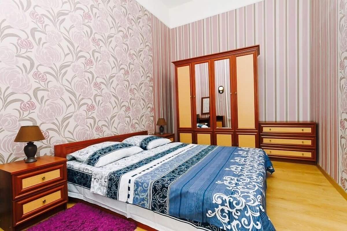 A bedroom with a bed, wooden nightstands, a dresser, and a mirror.