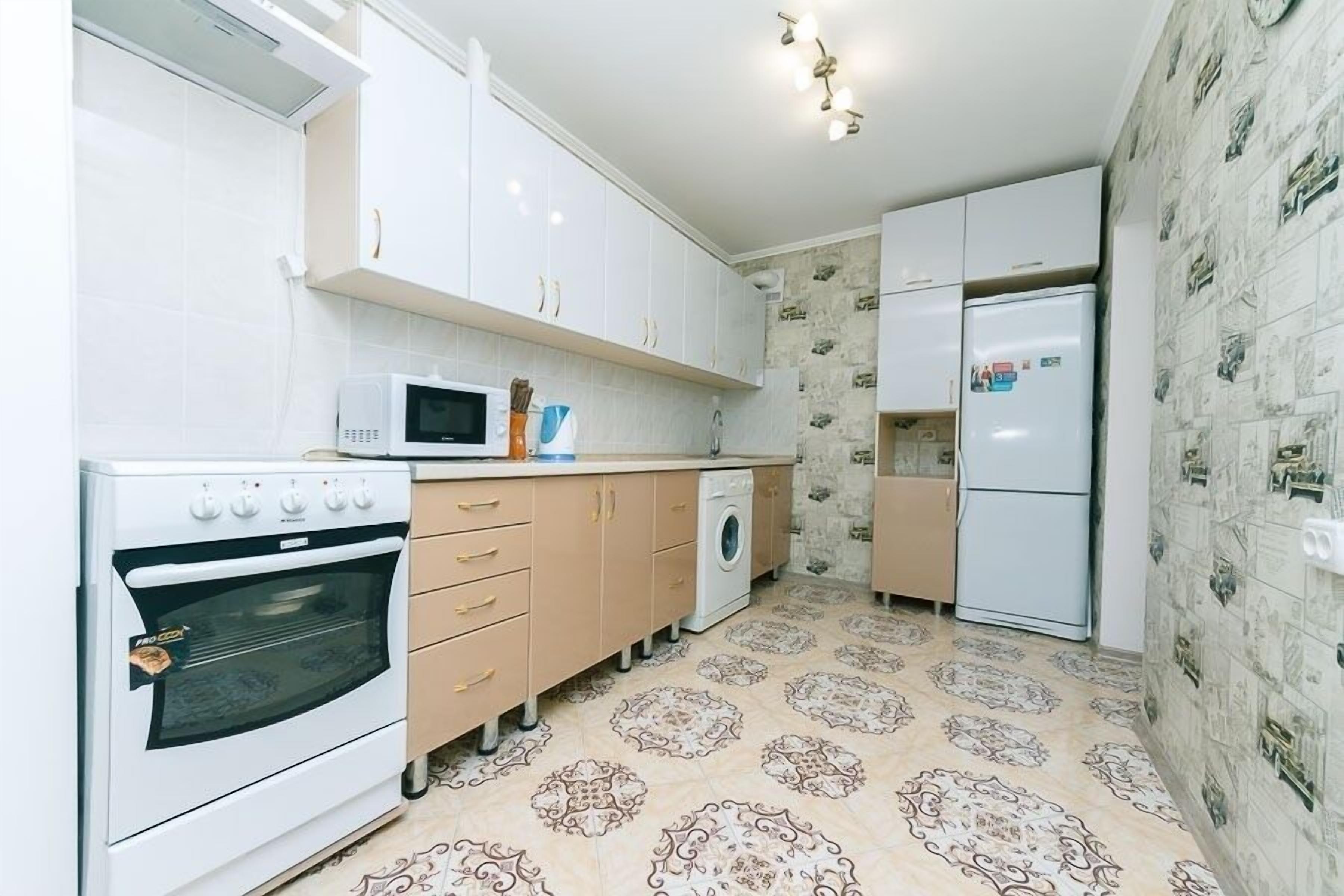 A compact kitchen with white cabinets, a microwave, a stove, a washing machine, and a refrigerator.