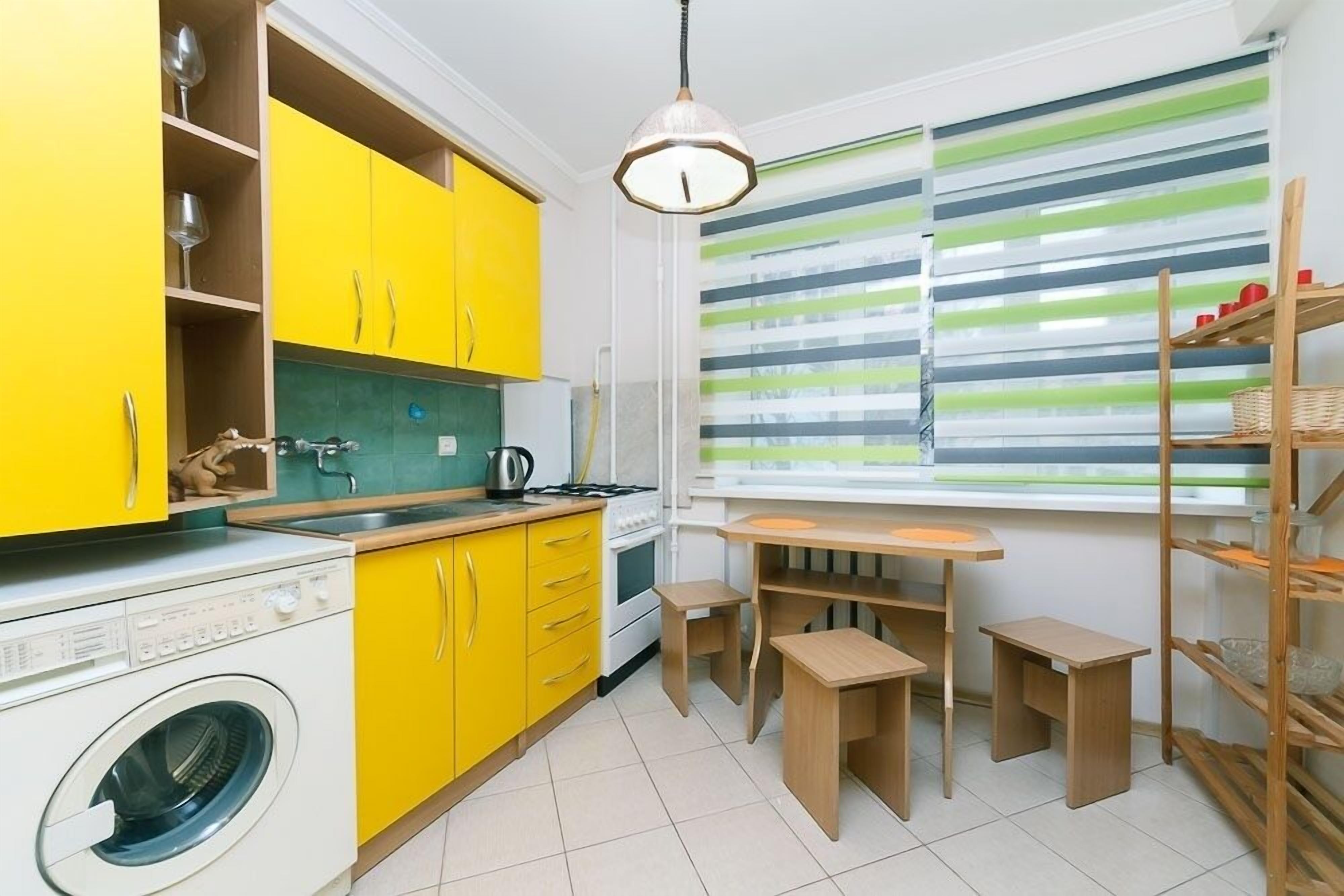 Una cocina compacta con armarios amarillos, una lavadora y un comedor con mesa y taburetes.