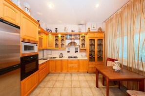 A kitchen with wooden cabinets, a stainless steel refrigerator, a microwave, a stove, and a dining table with a vase. - Hotrent Olympic (Kyiv)