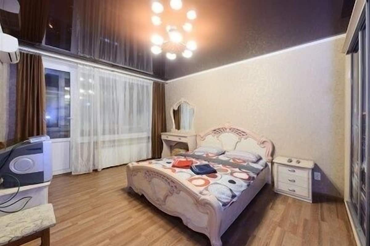 A bedroom with a bed, a dresser, a vanity, and a ceiling light fixture.
